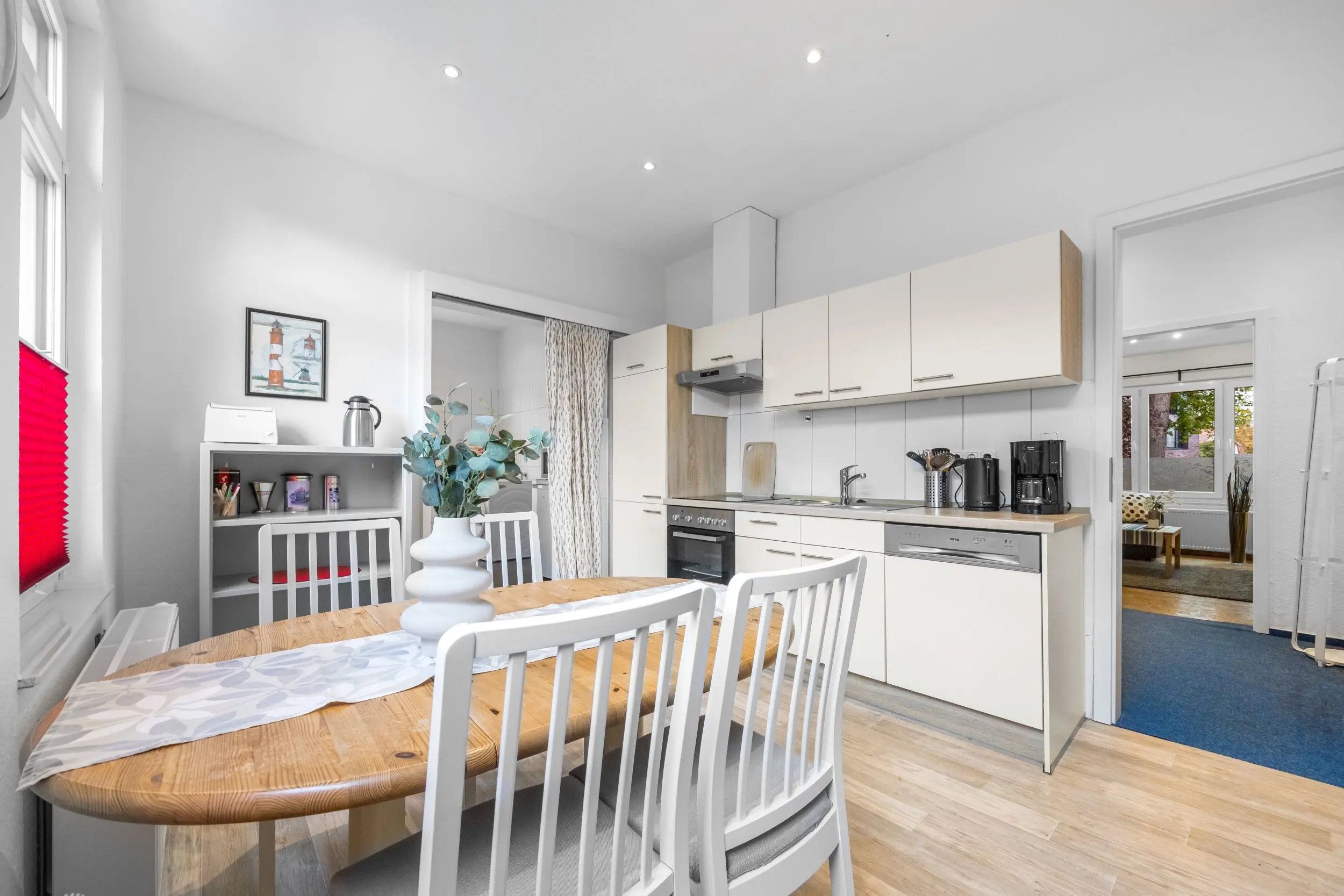 Open kitchen and dining area with white cabinets, stainless appliances, and a wooden table with white chairs.