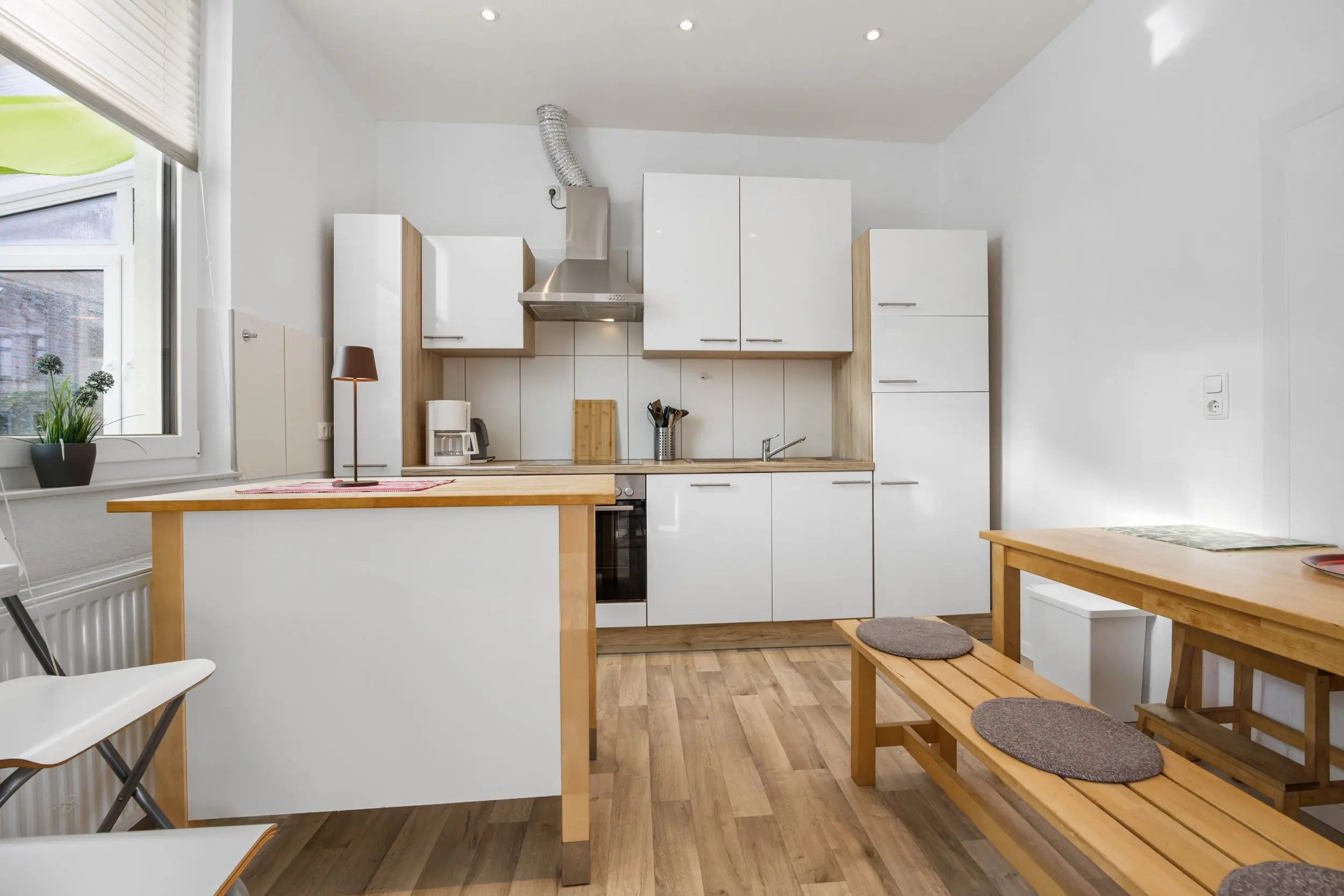 Bright modern kitchen with white cabinets, wooden countertops, and a breakfast island featuring benches and round cushions