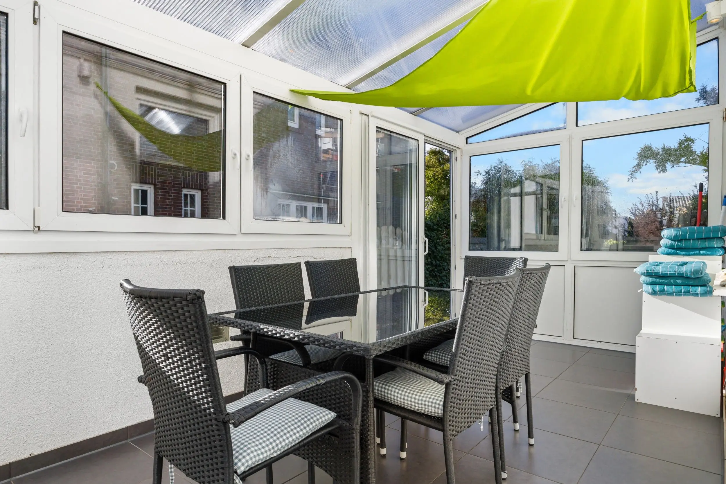 Enclosed patio with glass doors, black wicker dining chairs, and a bright lime-green awning.