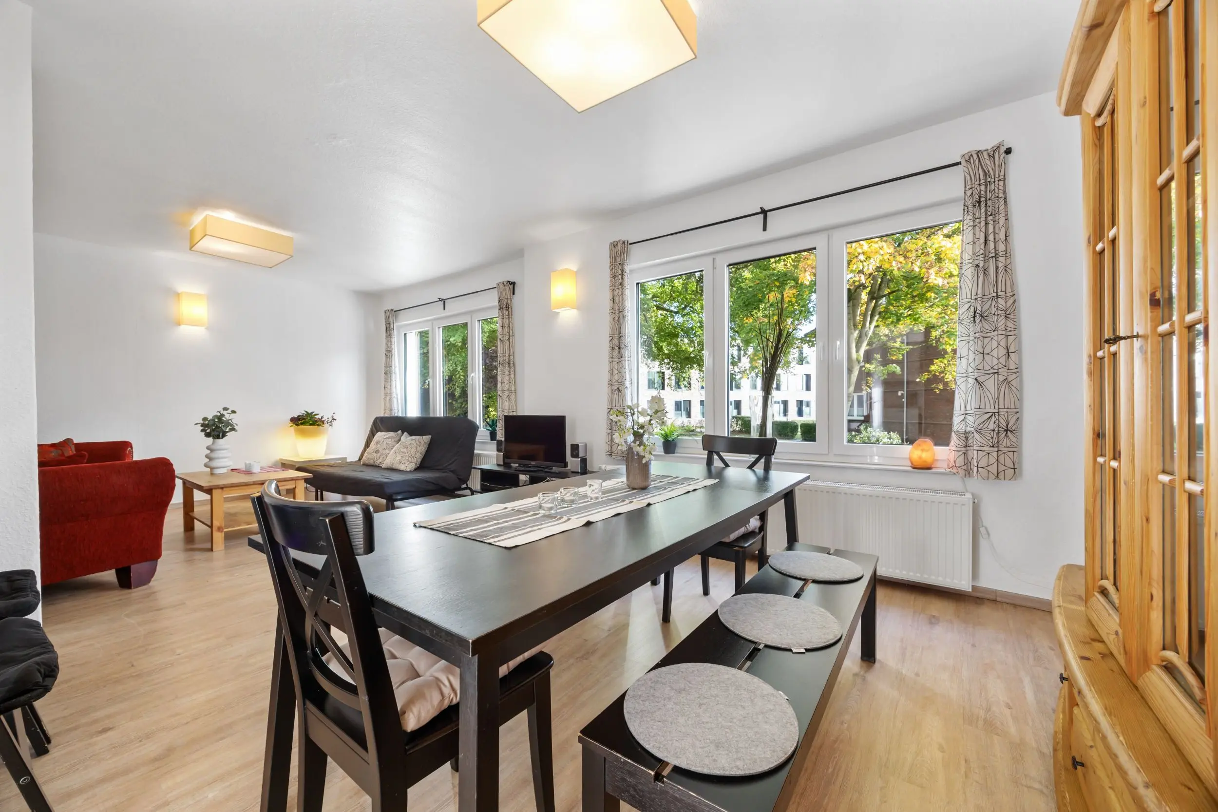 Open-plan living and dining room with a long black dining table, round gray placemats, and a red sofa visible in the background.