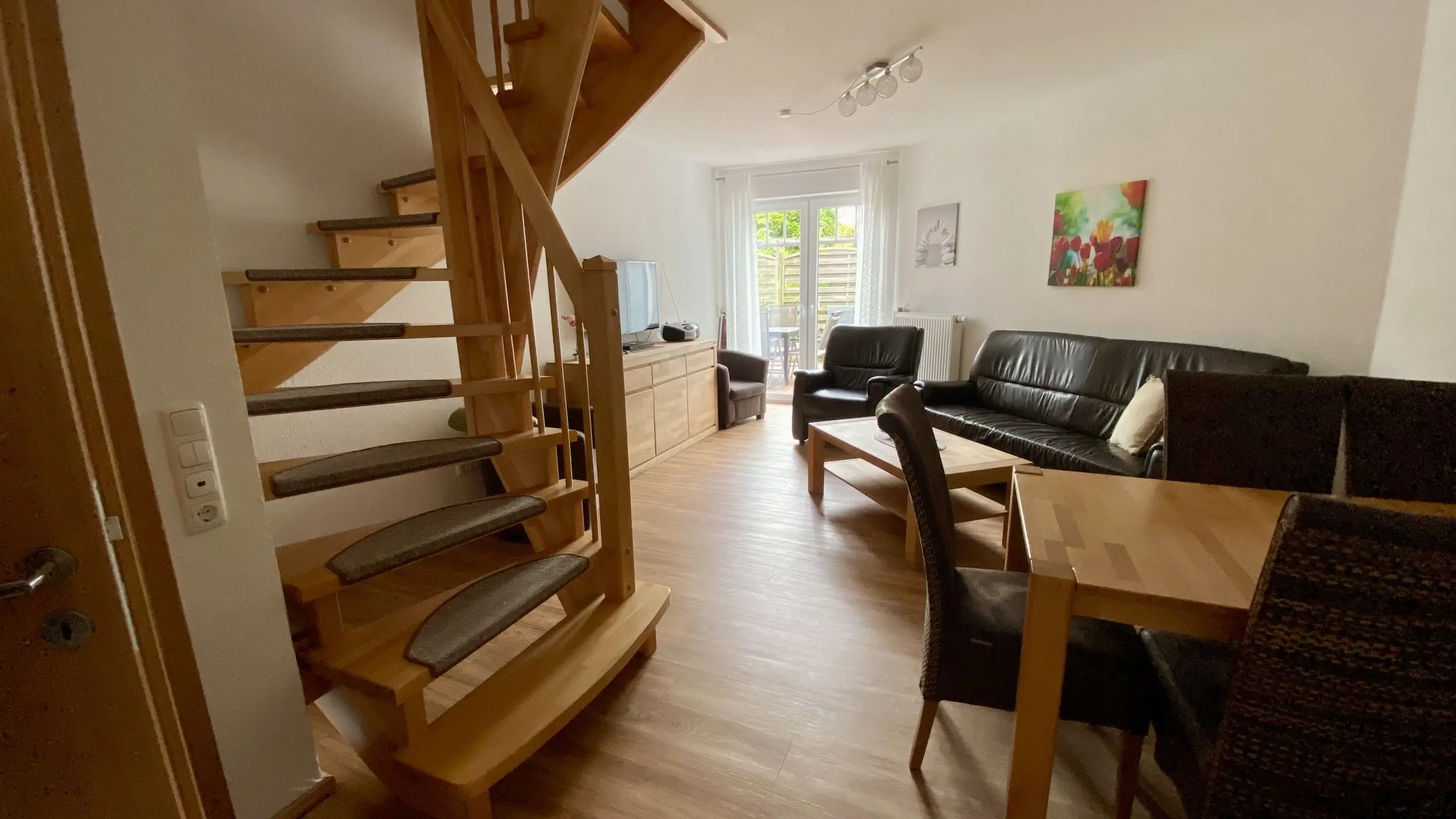 Living room with a wooden staircase on the left, leather sofa set, and a coffee table facing glass doors to an outside area.