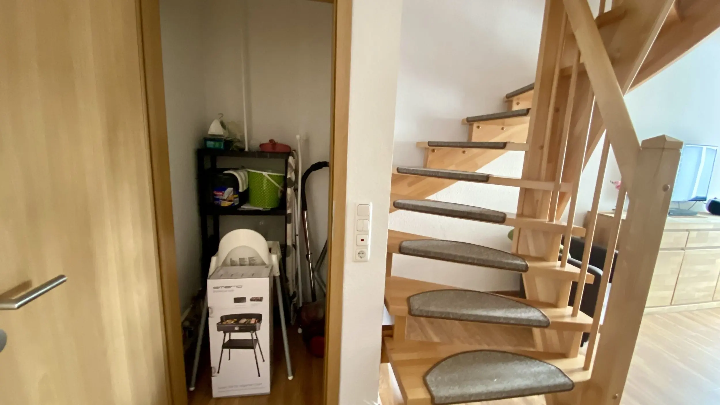 Interior view with a wooden spiral staircase on the right and a small storage closet filled with cleaning supplies on the left.