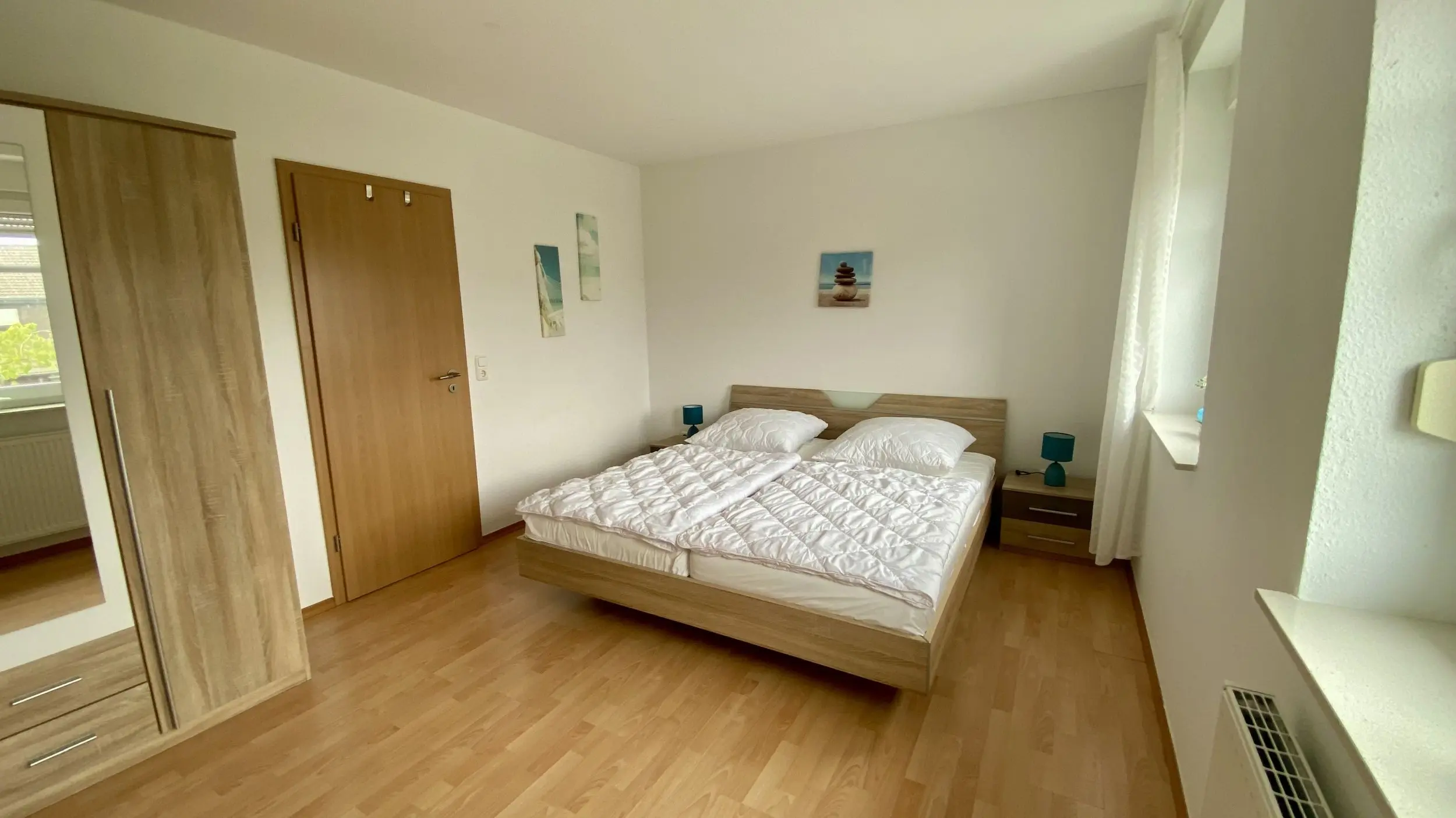 Bright bedroom with a double bed, wooden bed frame, and two teal bedside lamps on matching nightstands