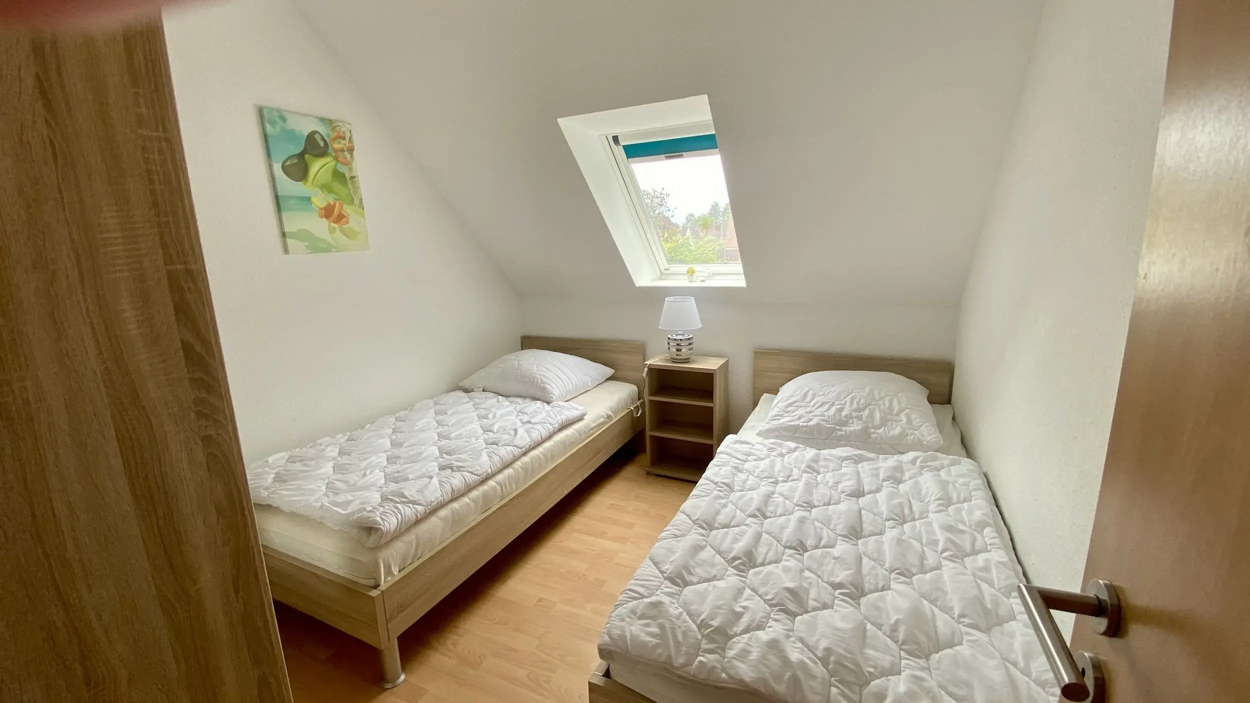 Twin bedroom with two single beds along opposite walls, a small nightstand and lamp between them, and a skylight window overhead.