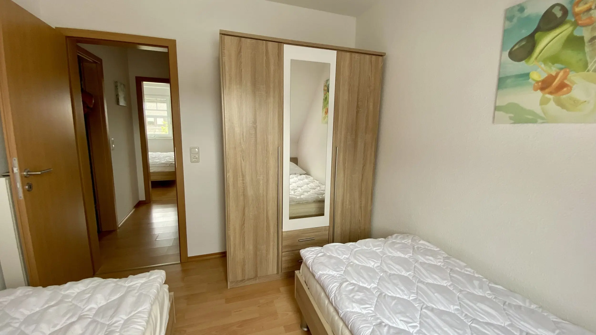 Small bedroom with two single beds, white quilts, a wooden wardrobe with a mirrored door, and a colorful wall art piece.