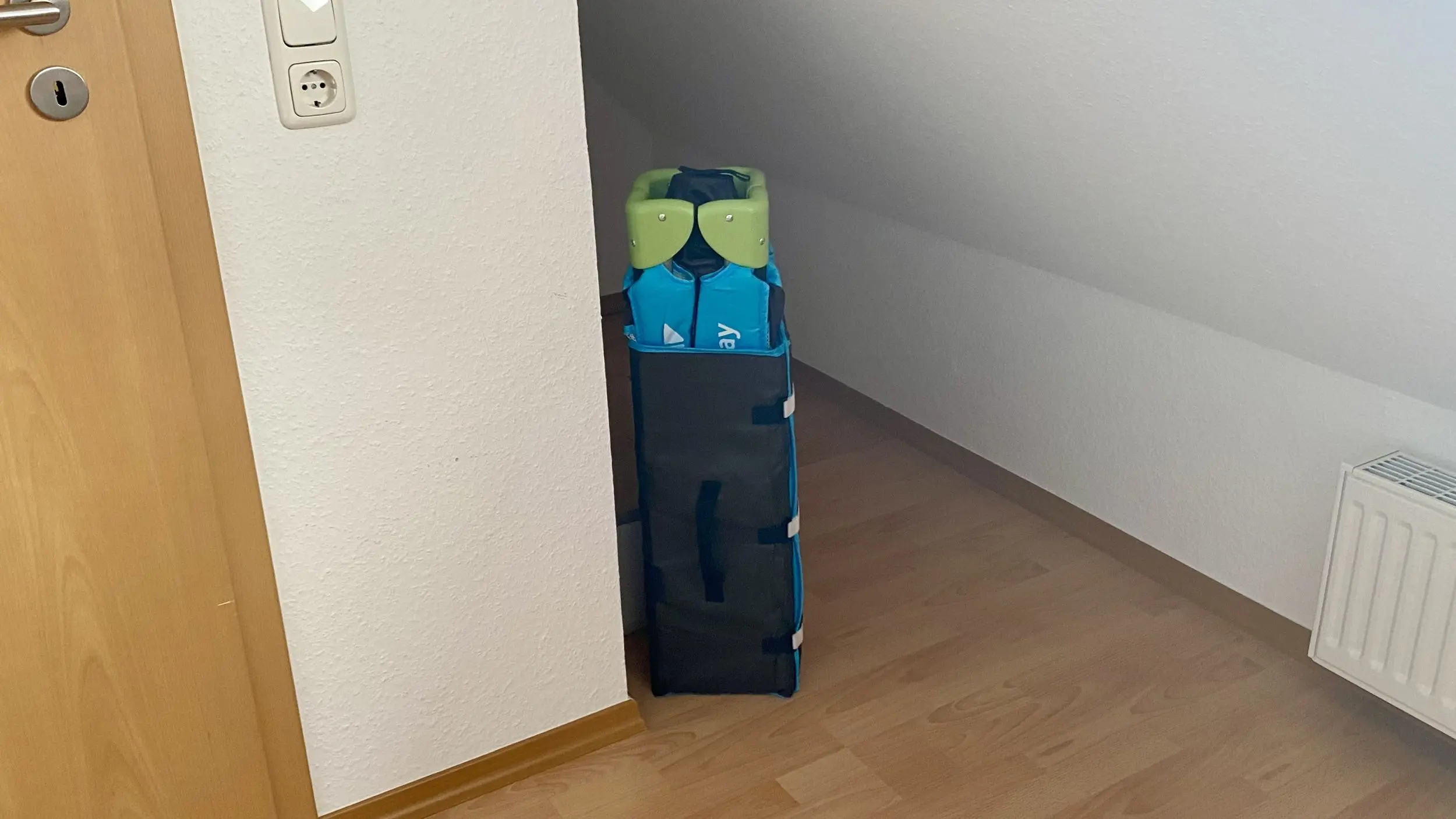 Blue and black rolling duffel bag standing upright in a narrow hallway near a wall and door frame.