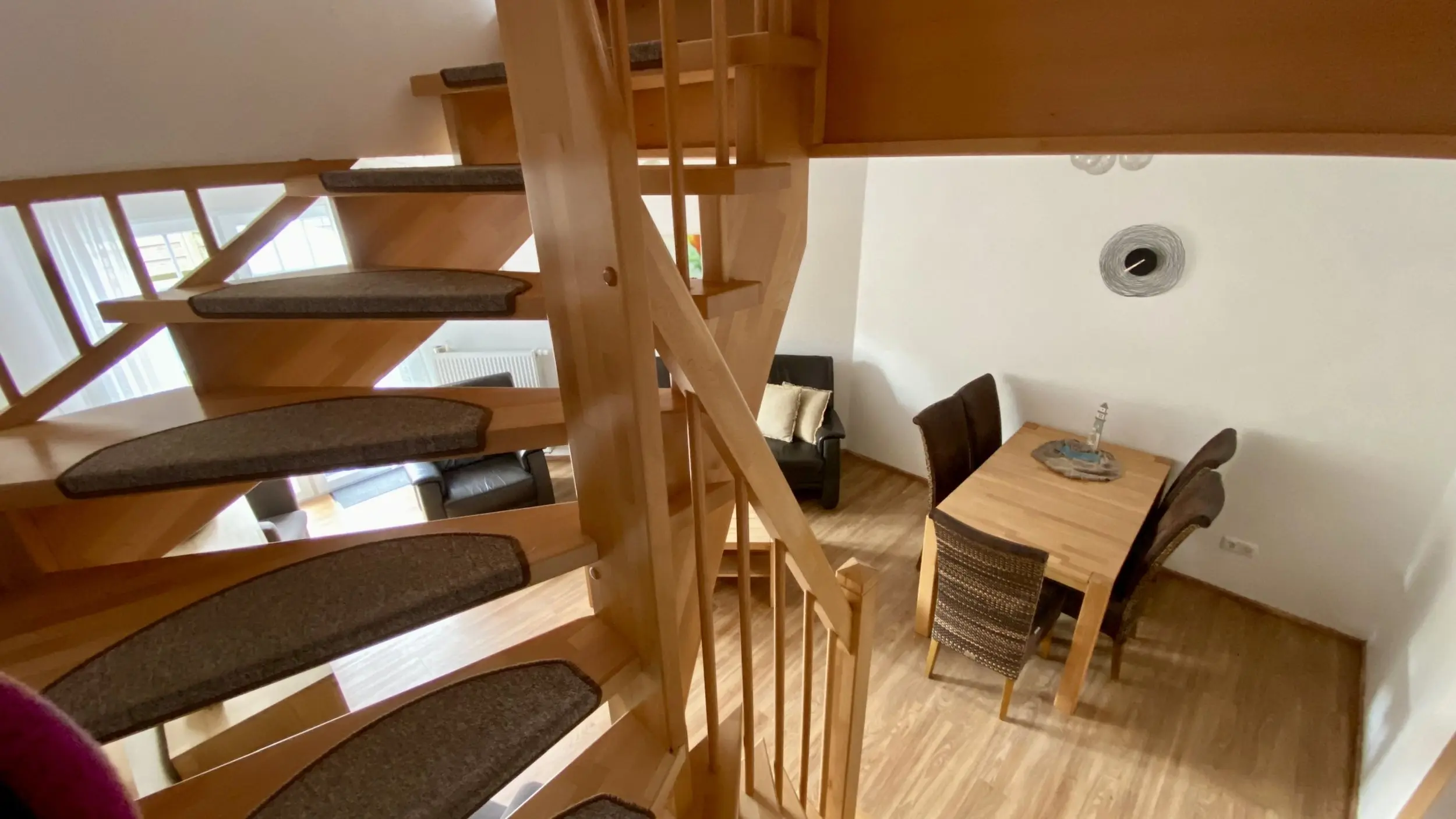 Wooden spiral staircase in a bright living/dining space with a dining table and chairs nearby.