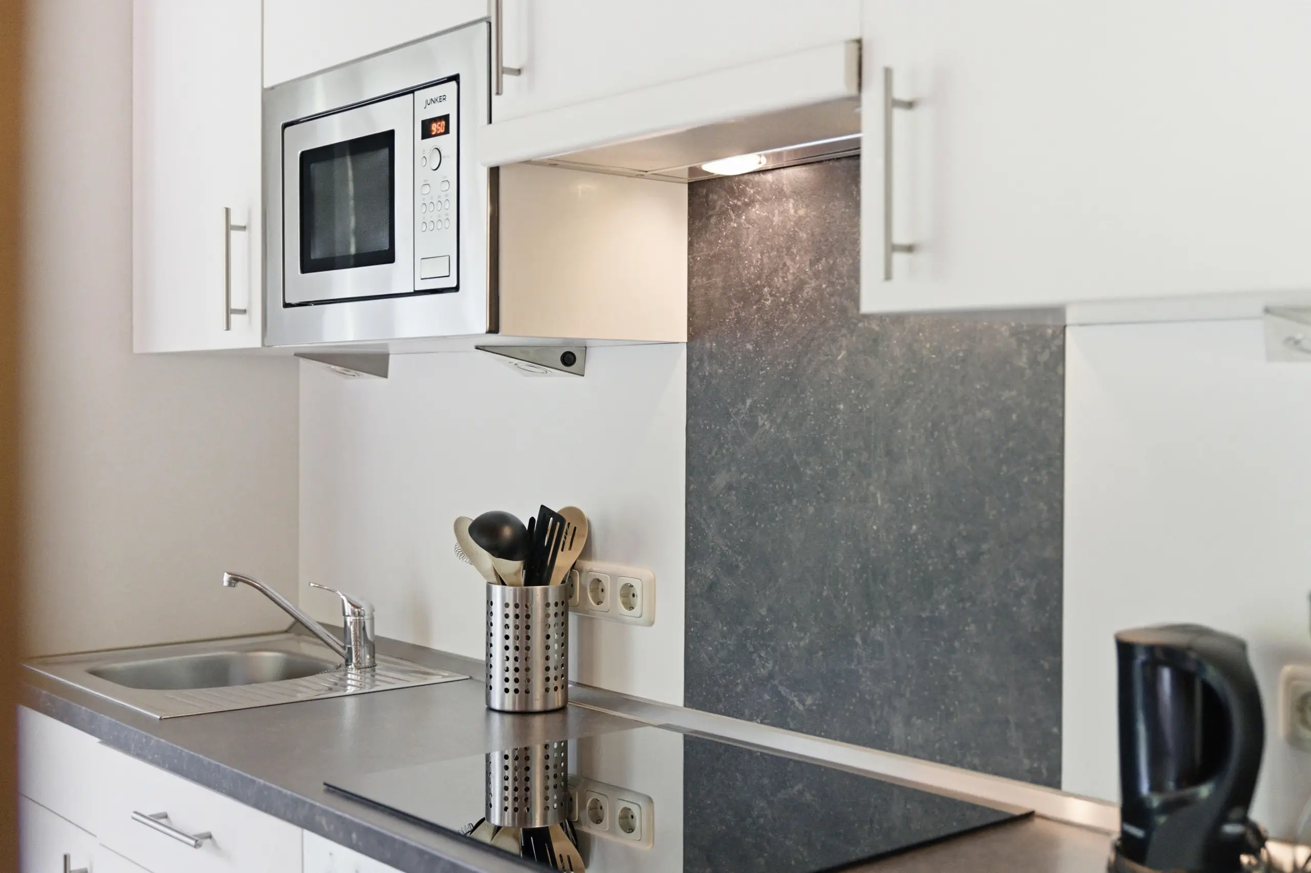 Modern kitchen counter with a stainless microwave built into white cabinetry above a sink area.
