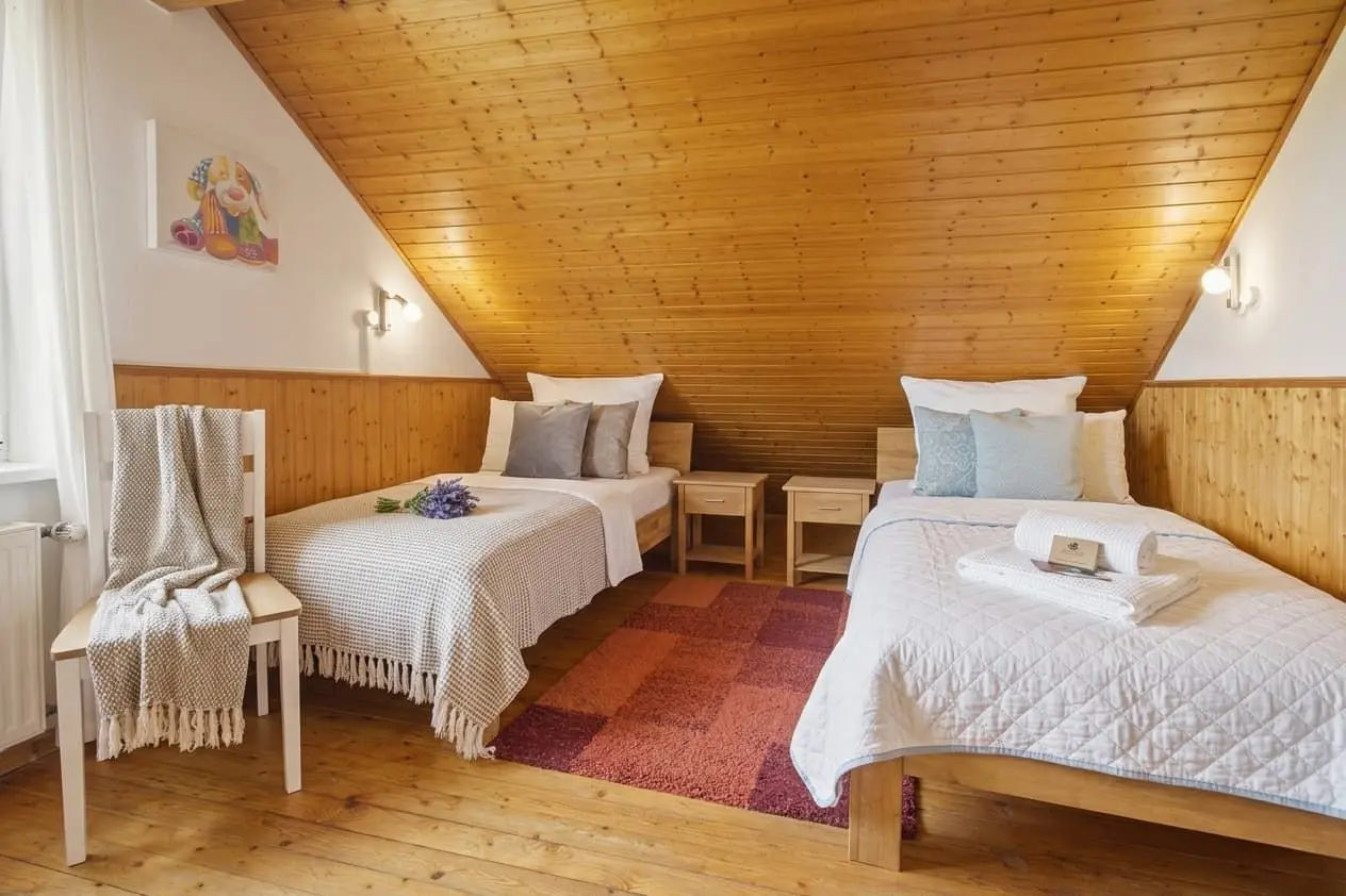 Twin bedroom in an attic with a slanted wooden ceiling, two single beds, white quilts, and bedside tables.