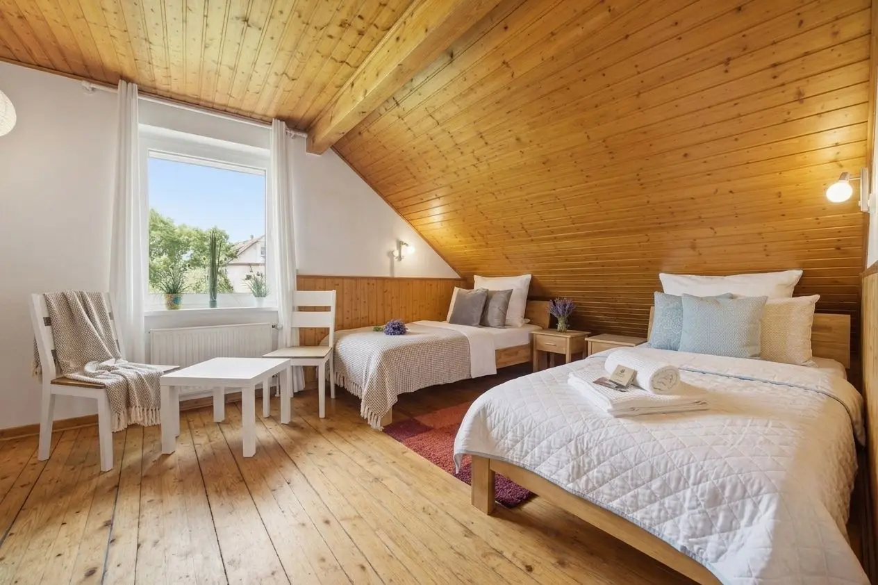 Cozy attic bedroom with two single beds, white quilts, and a window seat under a slanted wooden ceiling.