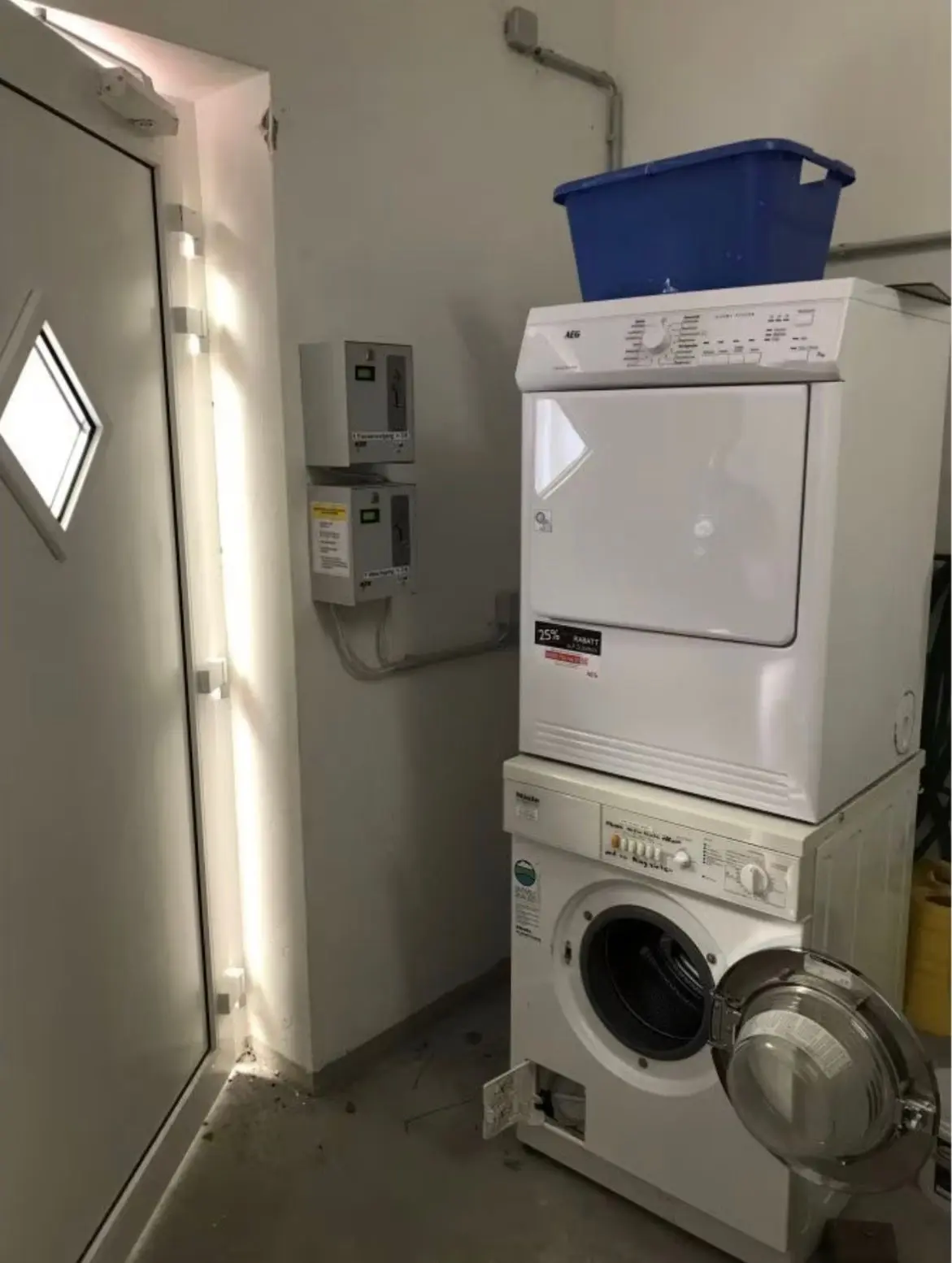 Stacked washer and dryer in a utility room, with a blue tub on top and a door to the left.