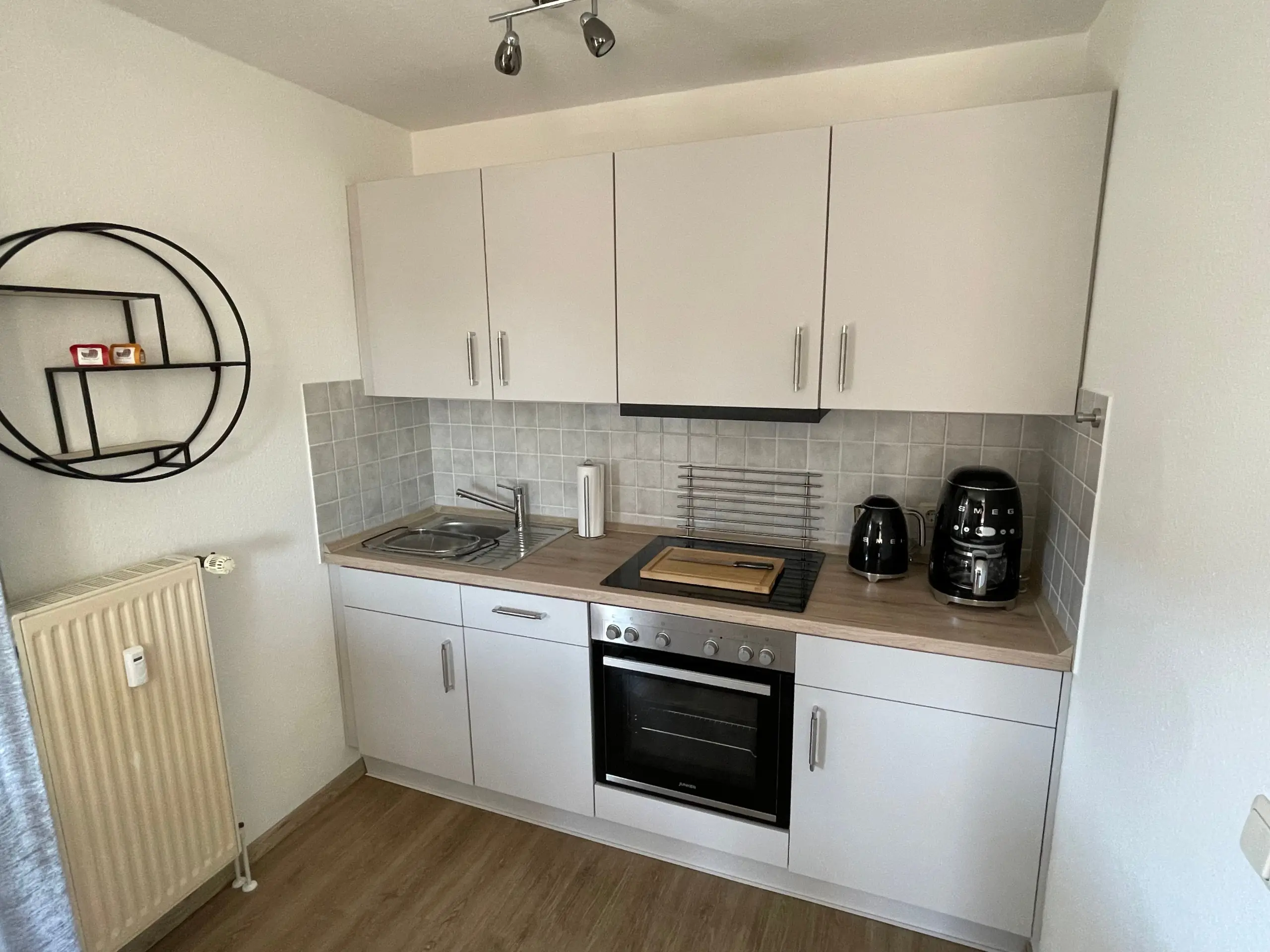 Compact kitchen with white upper cabinets, tiled backsplash, and stainless steel appliances (oven and stove).
