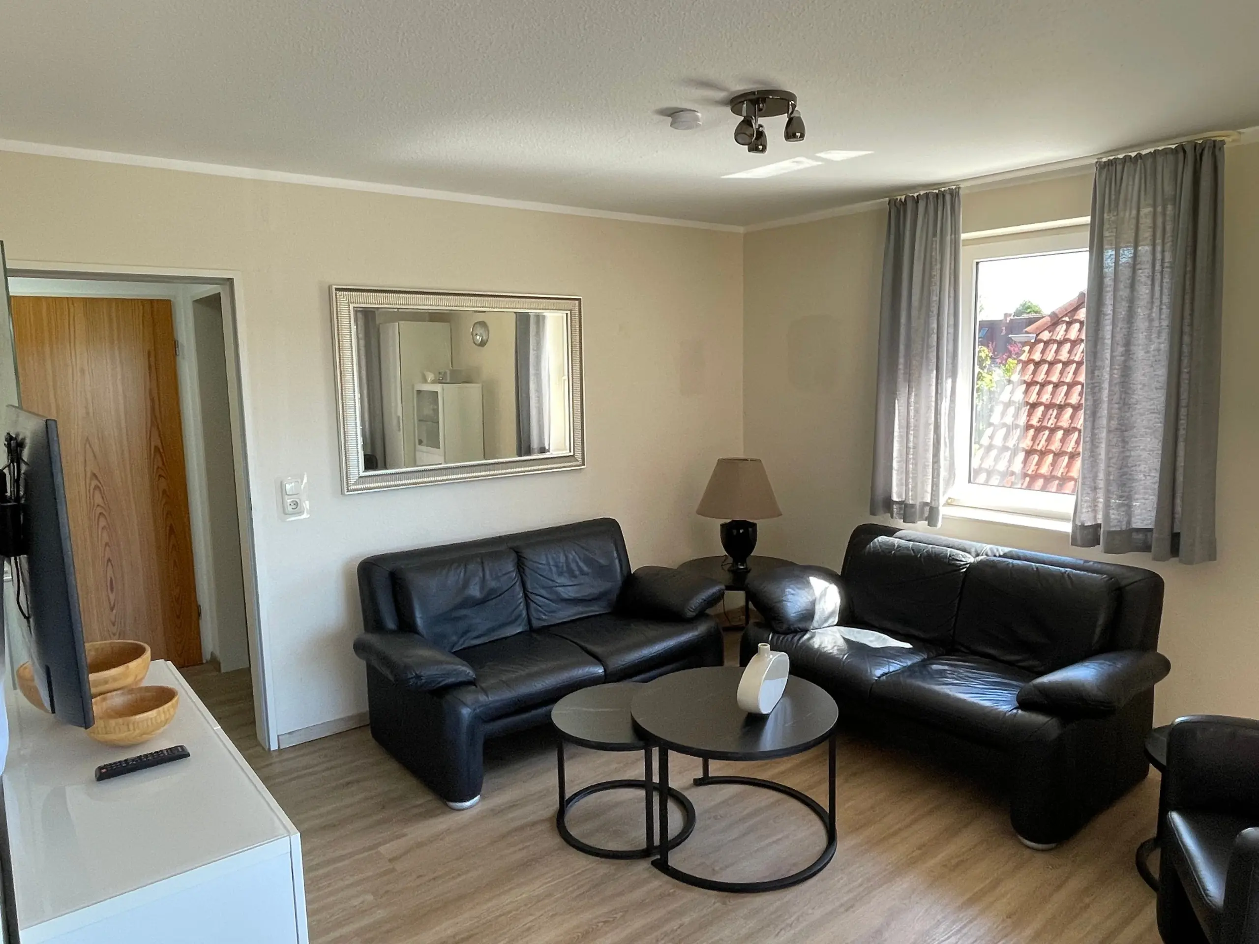 Living room with a black leather sectional, two round coffee tables, and a silver-framed mirror on a beige wall.