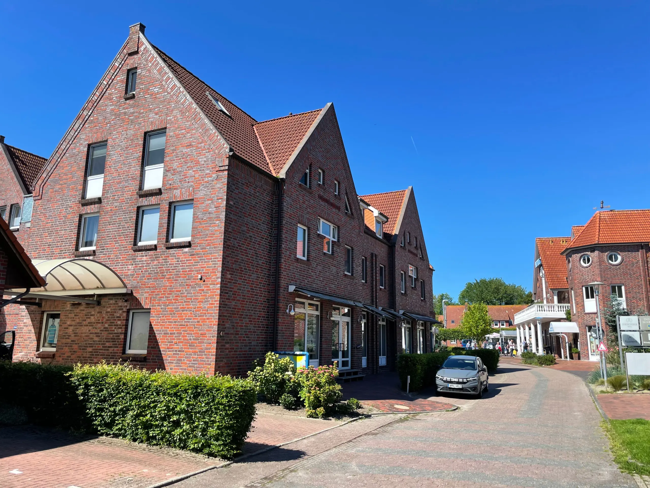 Brick townhouses with red tiled roofs along a sunny street under a clear blue sky.
