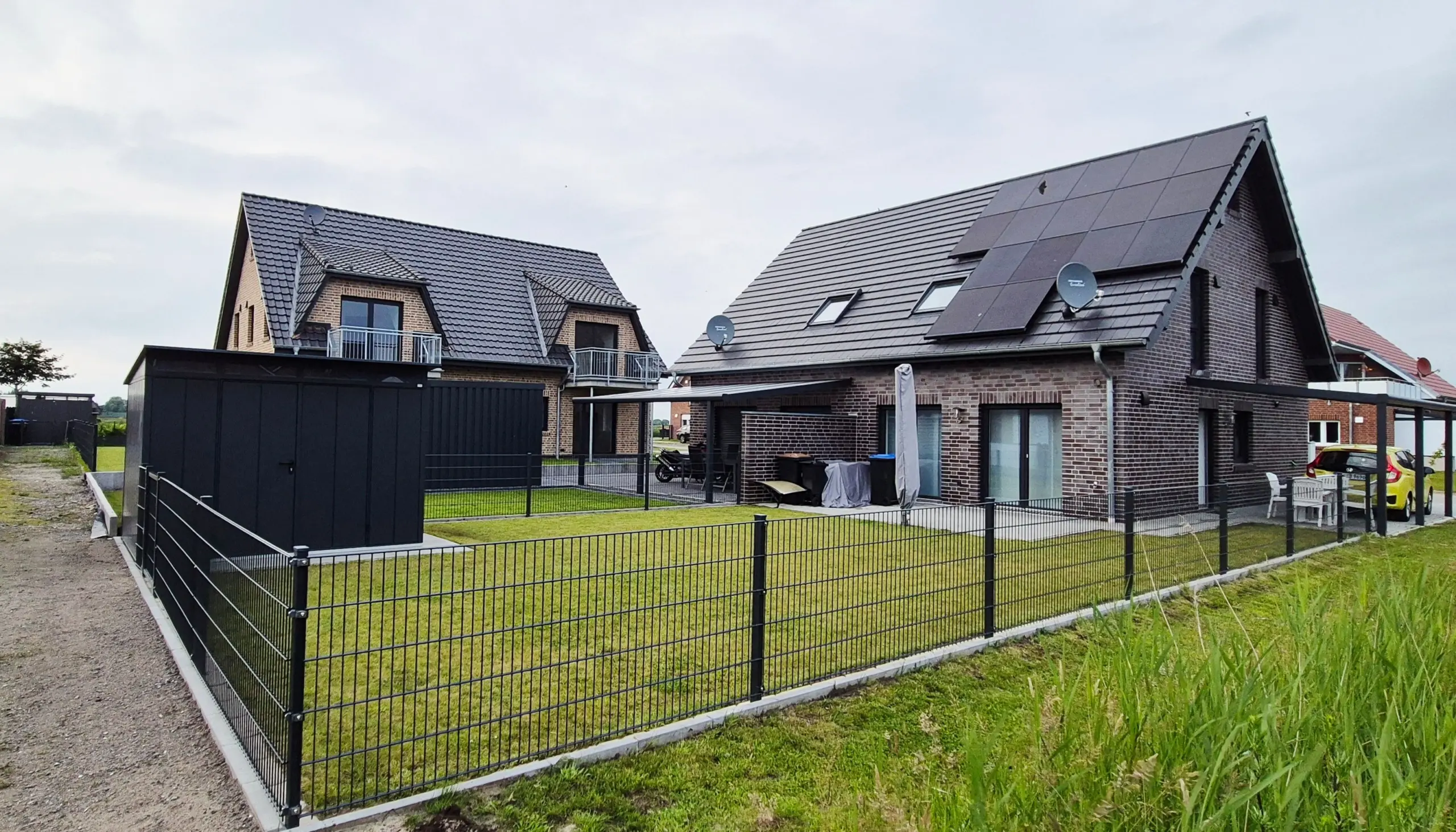 Modern brick houses with solar panels on sloped roofs and a fenced grassy yard in a suburban neighborhood