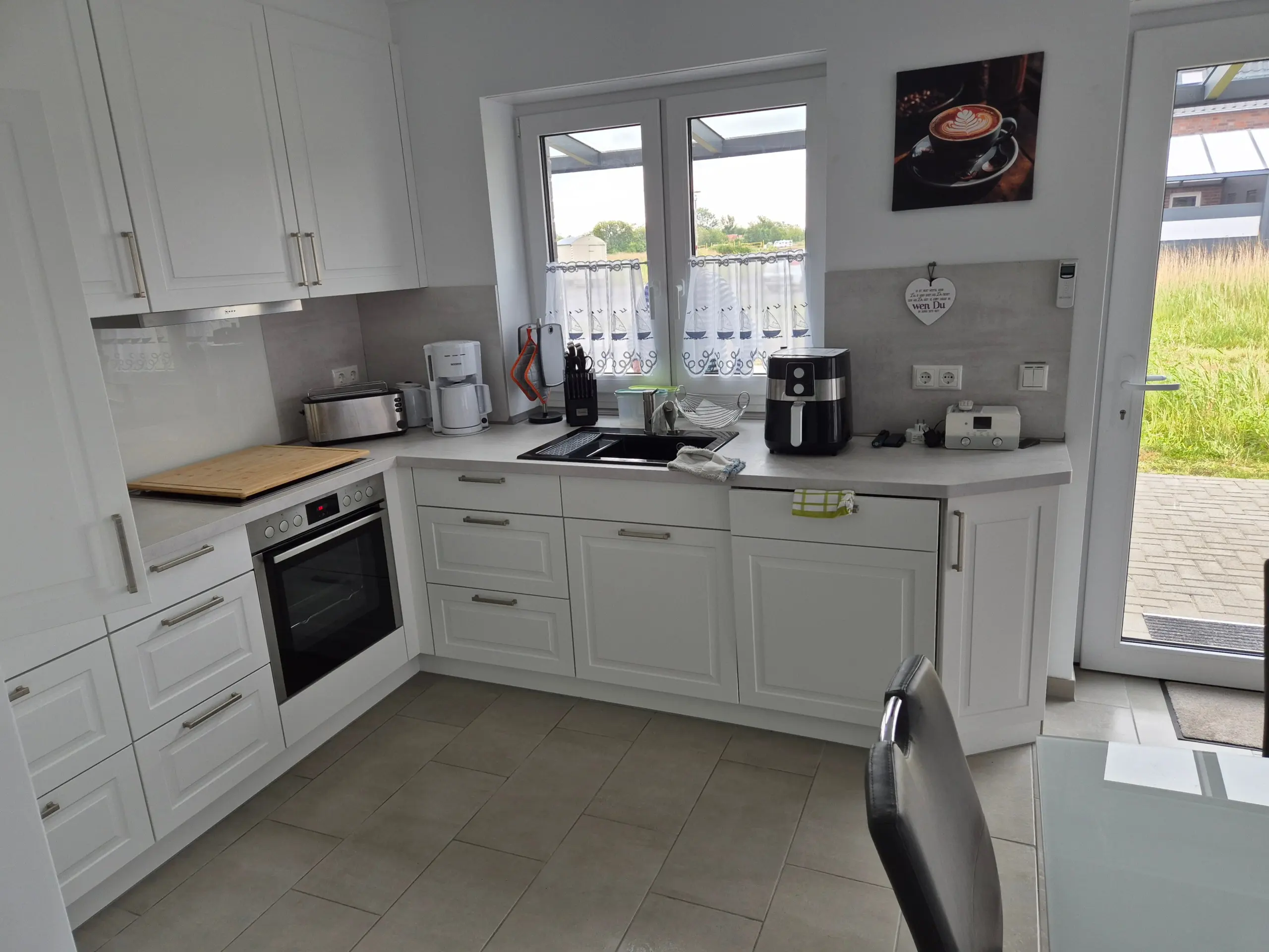Bright white kitchen with built-in oven, white cabinets, and small appliances on the counter by the sink. (informative)