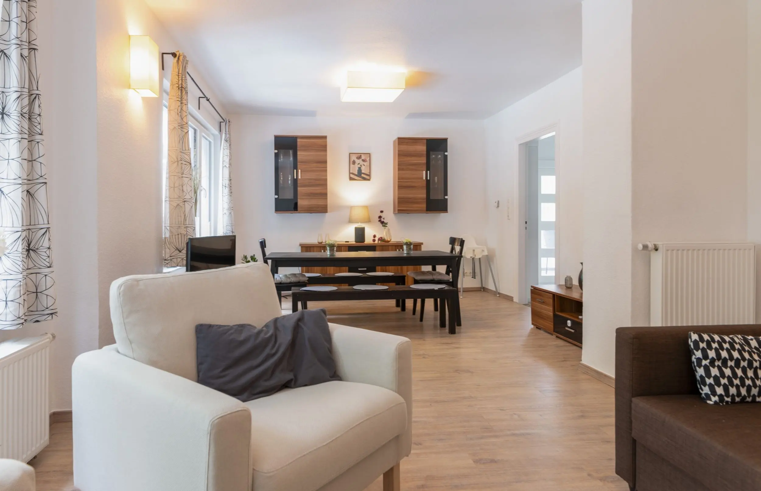 Open-plan living and dining area with cream sofa, dark dining table, wood cabinetry on the back wall, and soft ambient lighting.