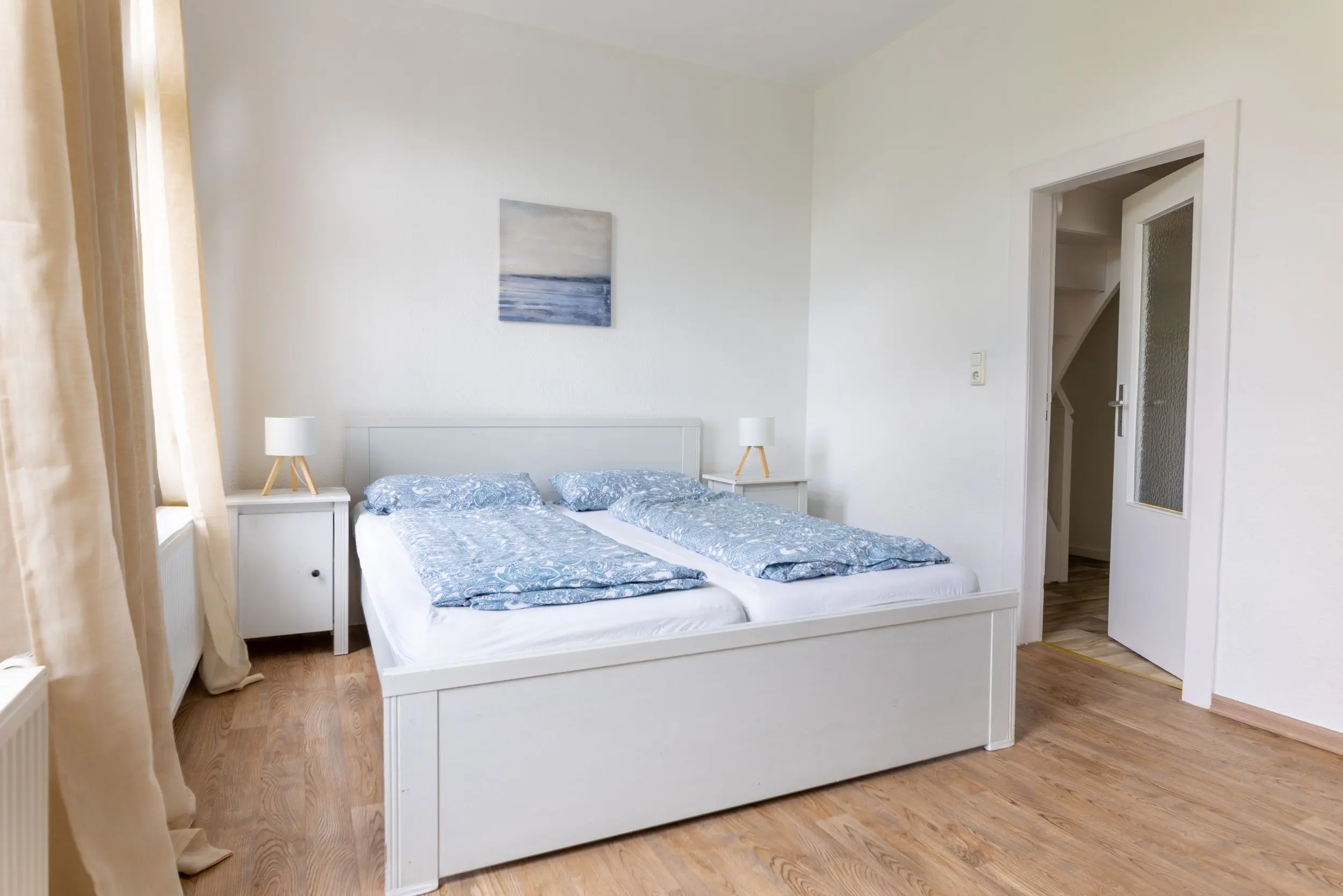 Bright white bedroom with two single beds pushed together, blue patterned bedding, white nightstands and lamps on either side.