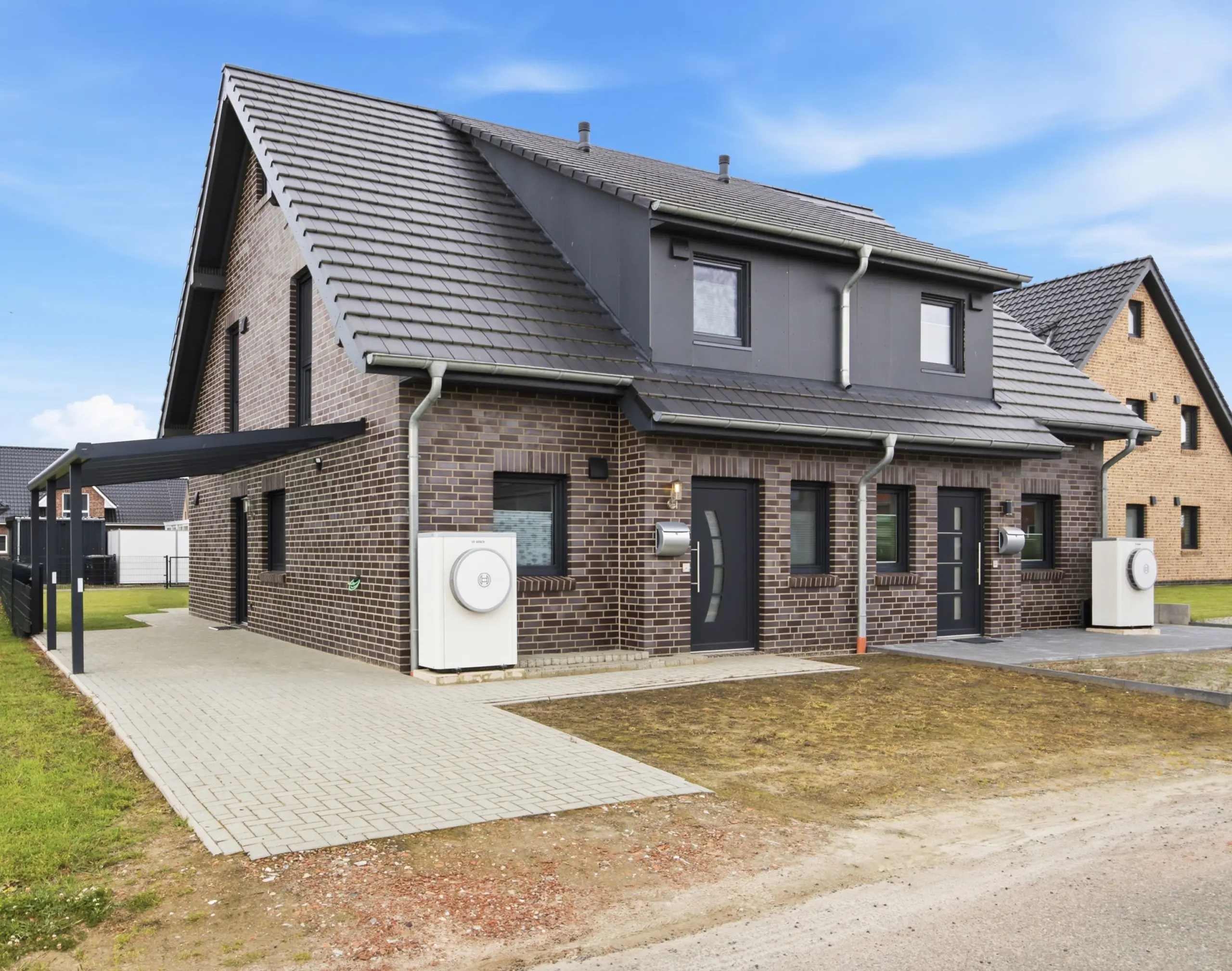 Two-story brick house with a dark gray slate roof, dormer windows, and a paved walkway along the front yard.