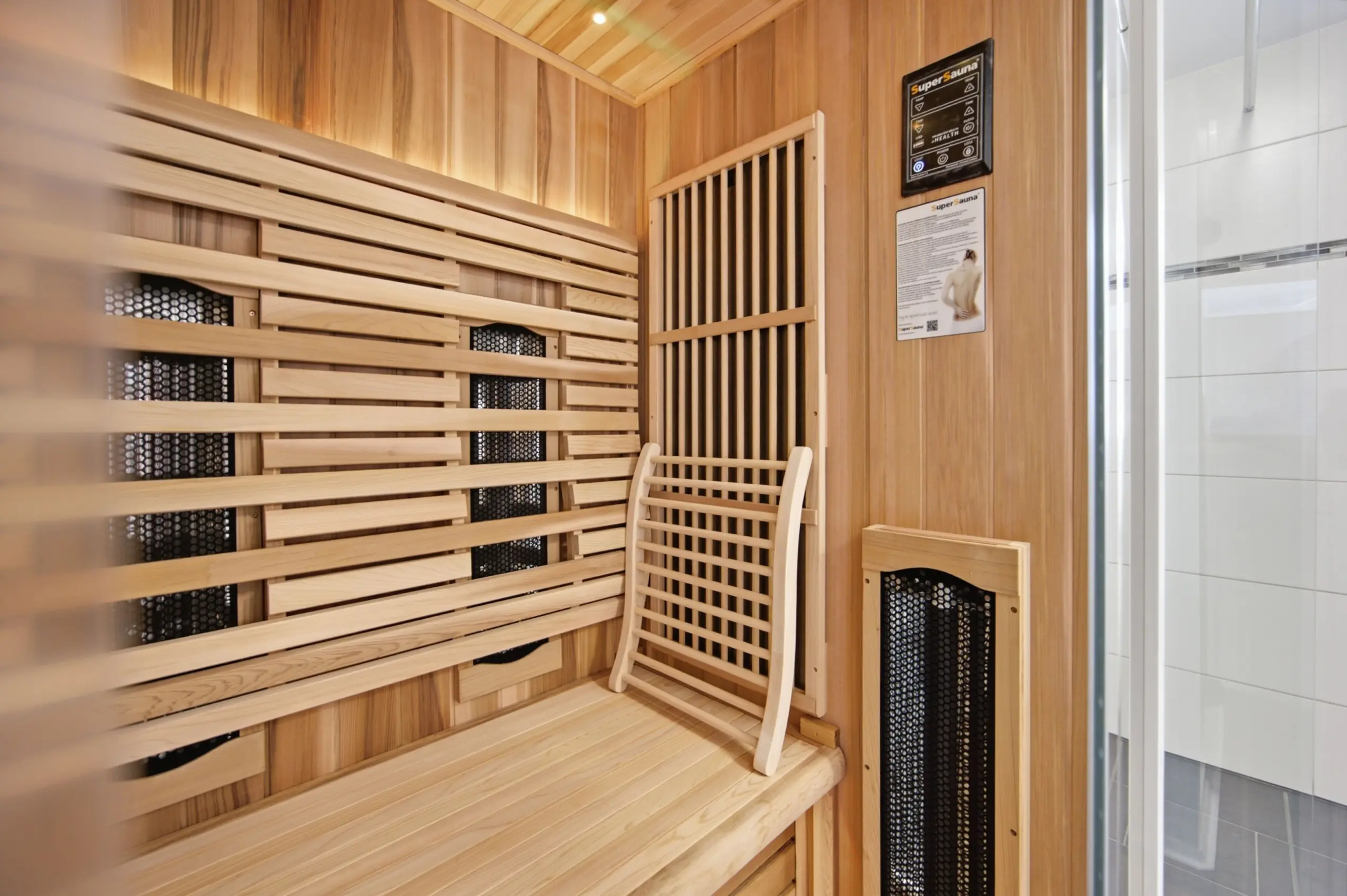 Wooden sauna interior with tiered benches, warm wood panels, and a heater at the back wall near a slatted door.
