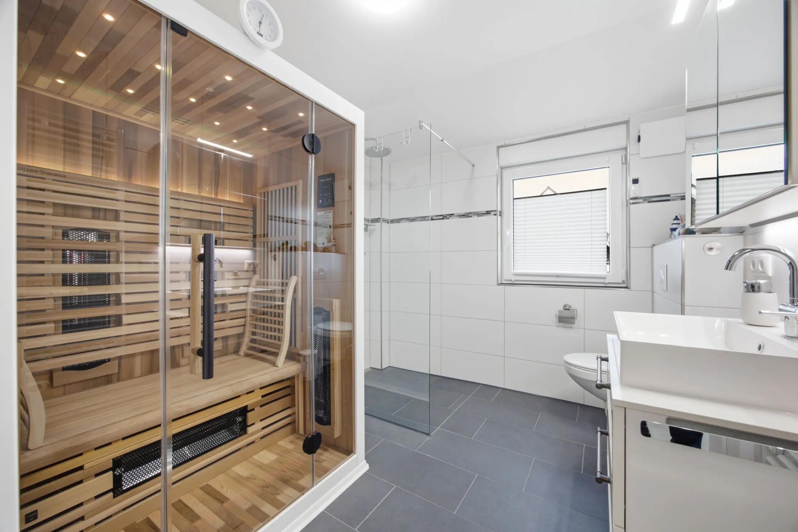 Modern bathroom with a glass-walled sauna on the left and white tiled walls on the right with a sink area nearby