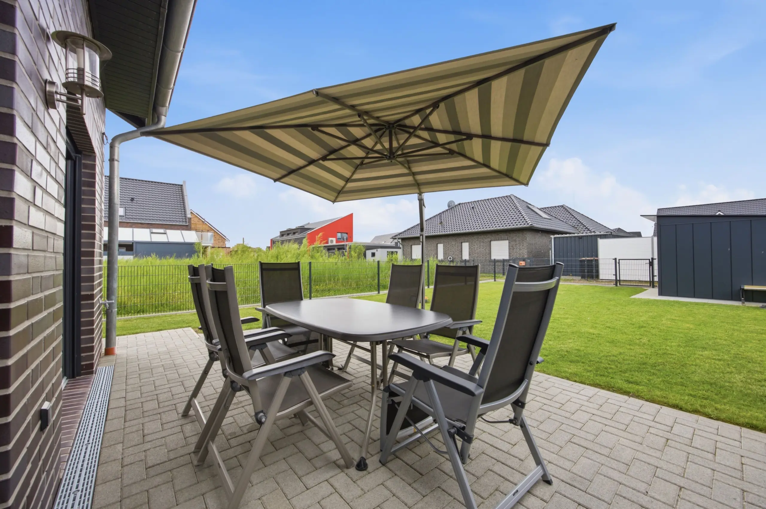 Patio dining set under a large striped beige-and-green umbrella in a sunny backyard.