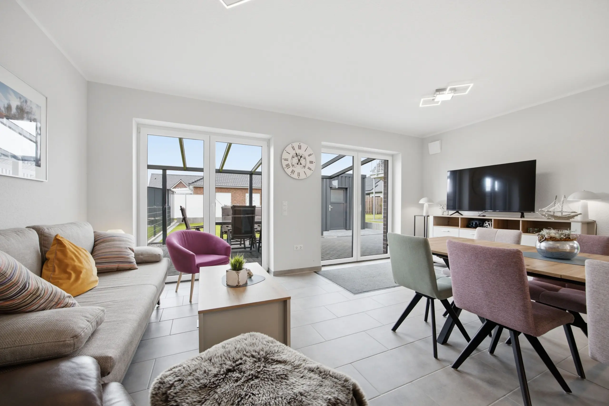 Bright modern living room with a grey sectional sofa, yellow cushions, and glass doors opening to a patio outside.