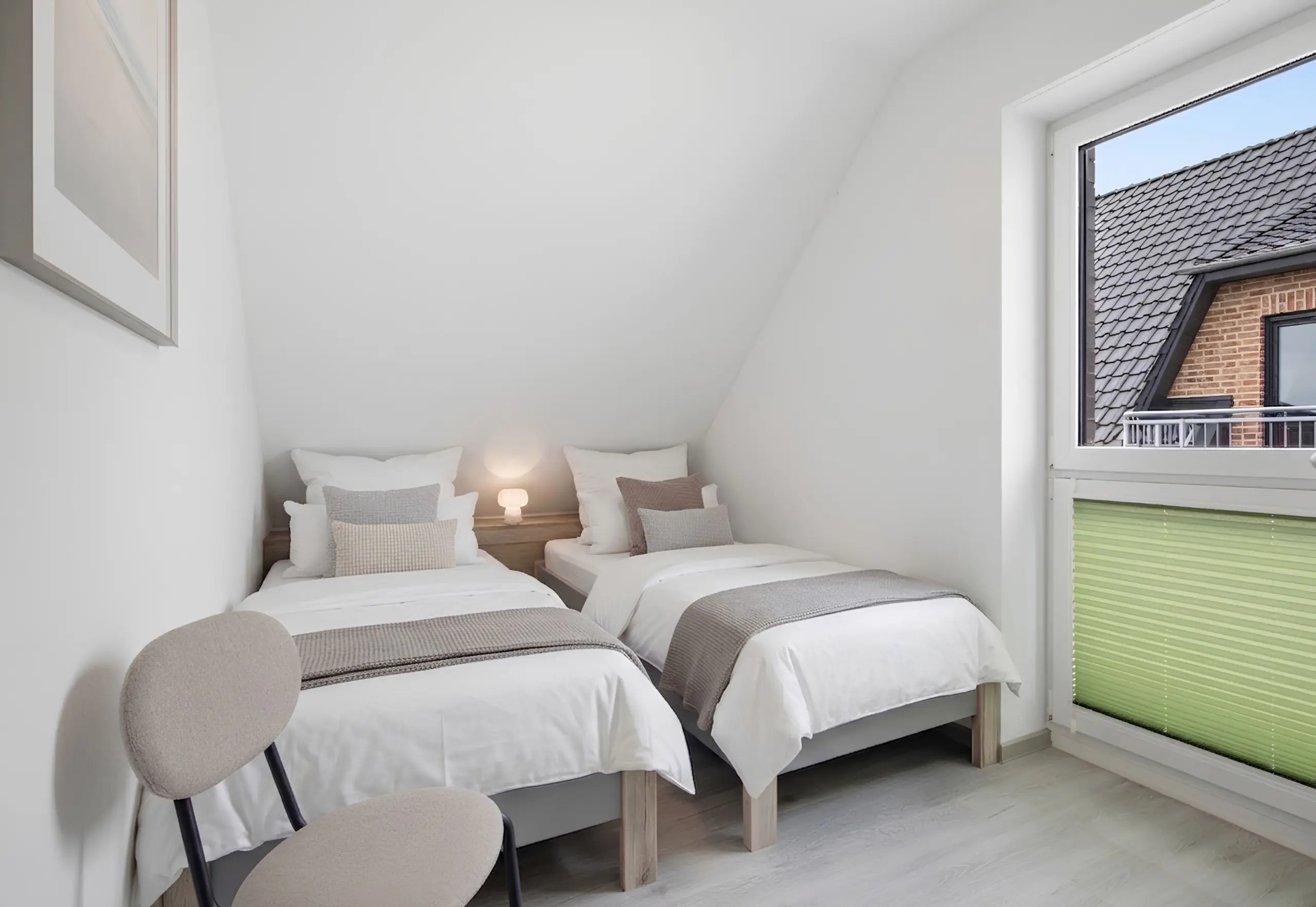 Attic bedroom with three neatly made single beds, white linens and gray-beige pillows, and a small bedside lamp between them.