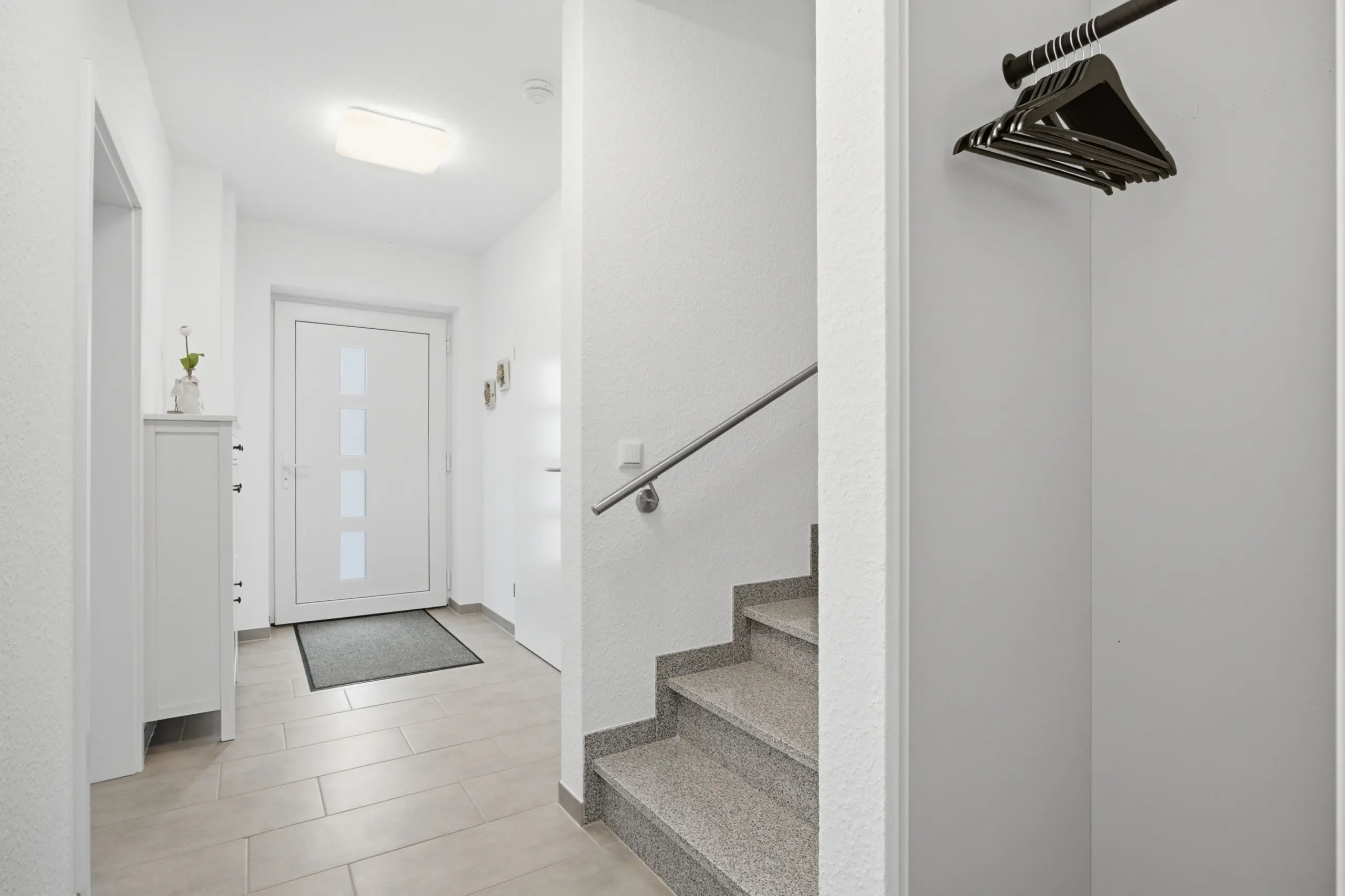 Bright white entry hall with a front door that has four frosted glass panels; stairs on the right and a row of black hangers on a rail.