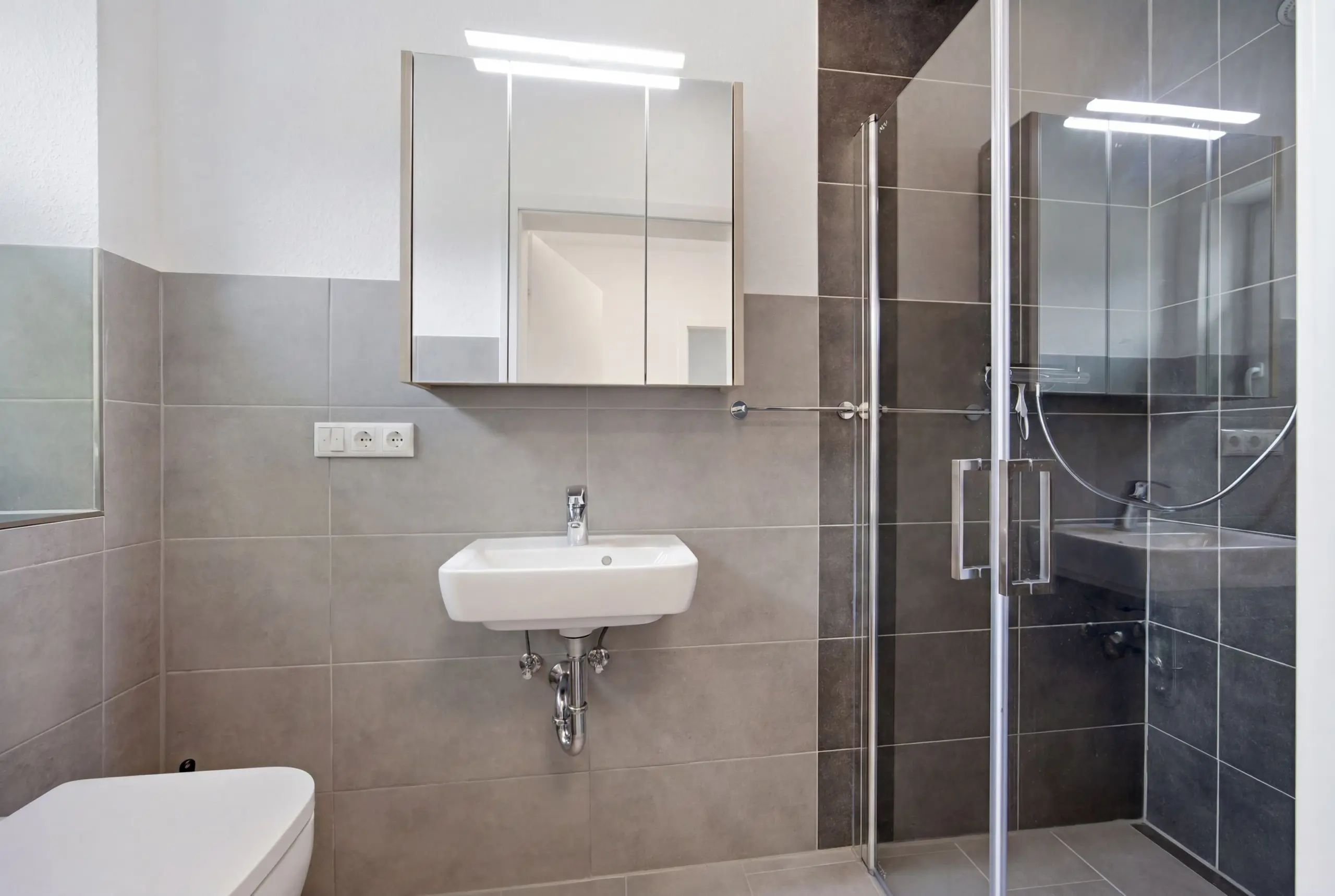 Modern bathroom with wall-mounted sink, mirrored cabinet, and glass shower enclosure with chrome fixtures.