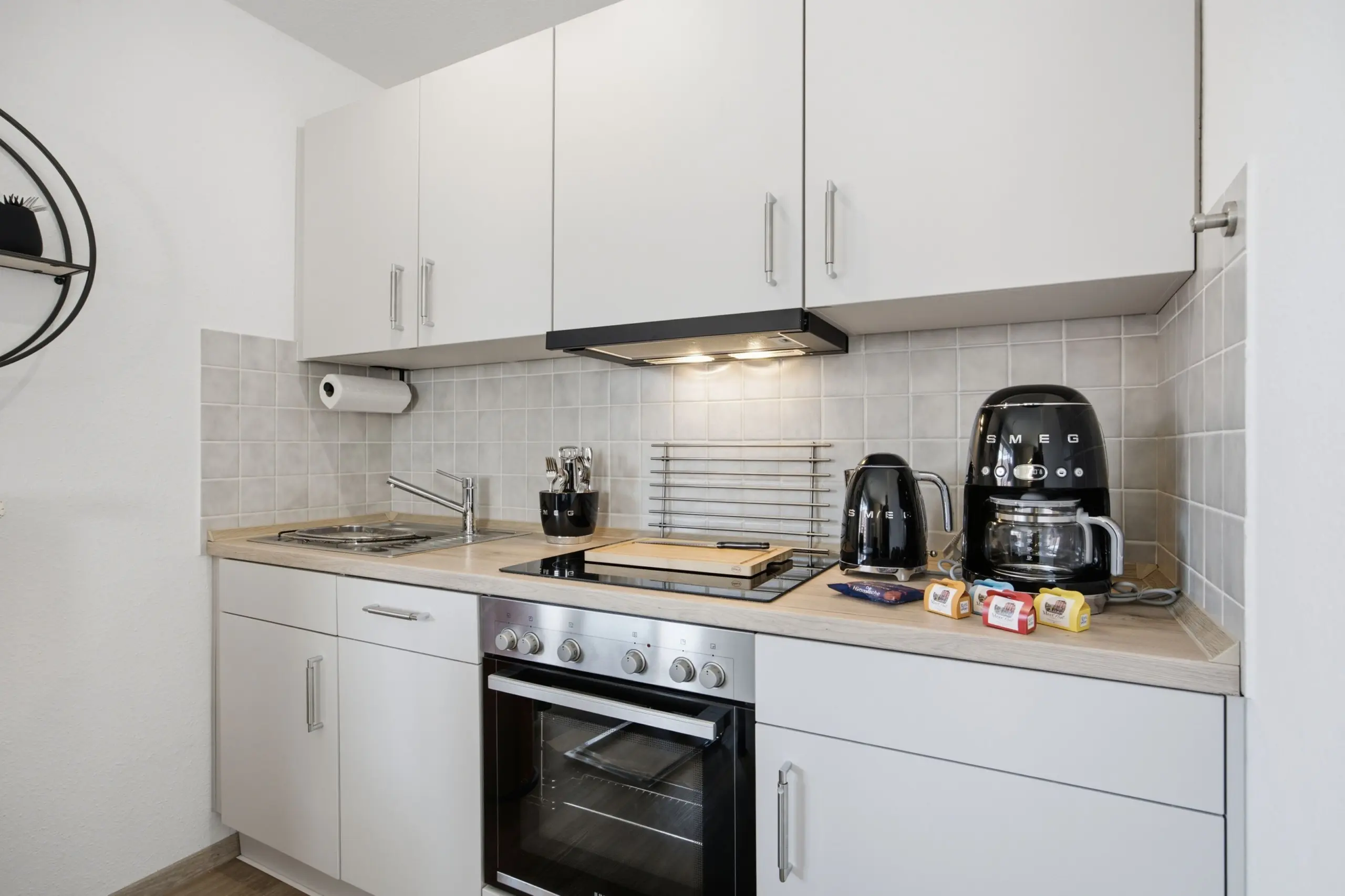 Modern white kitchen with built-in oven, stainless steel range hood, and cabinets above the counter.