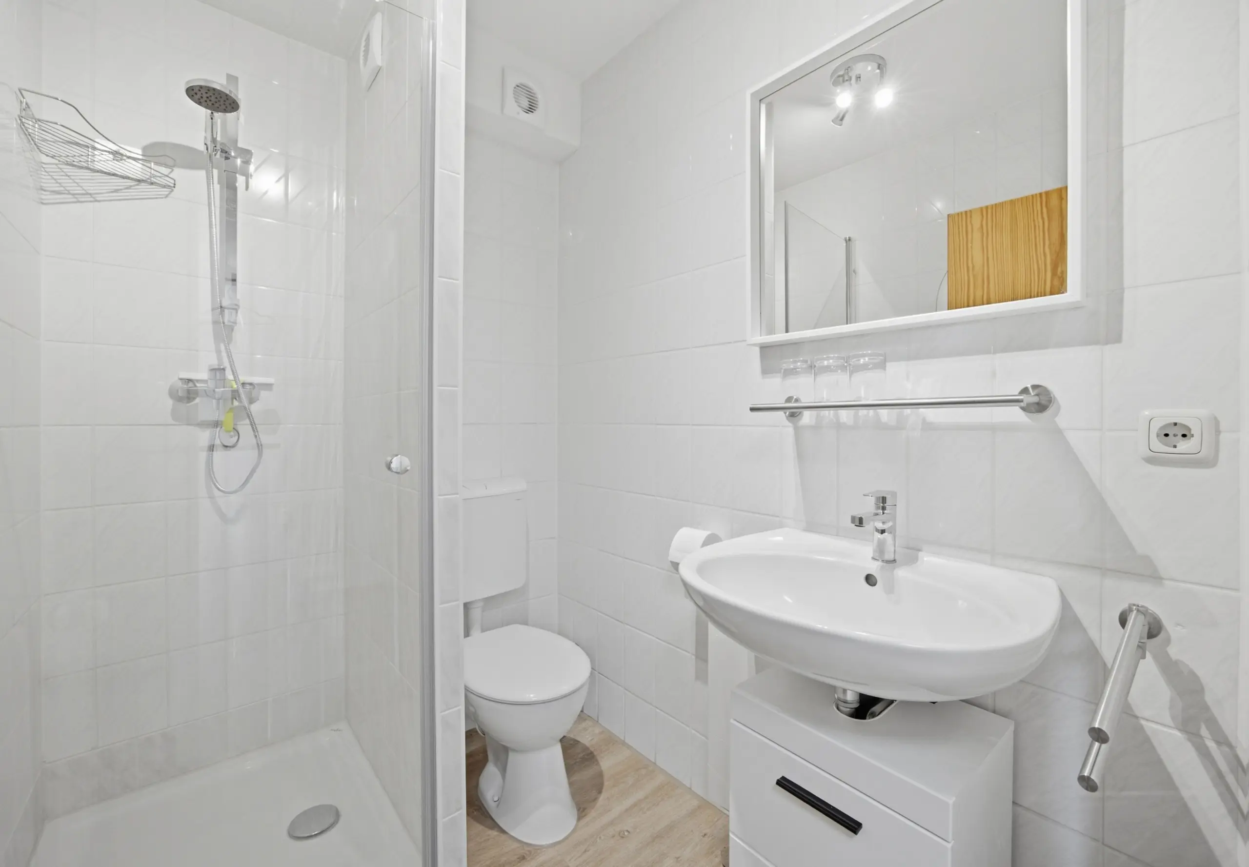 Modern white bathroom featuring a glass shower enclosure, pedestal sink, wall mirror, and toilet.