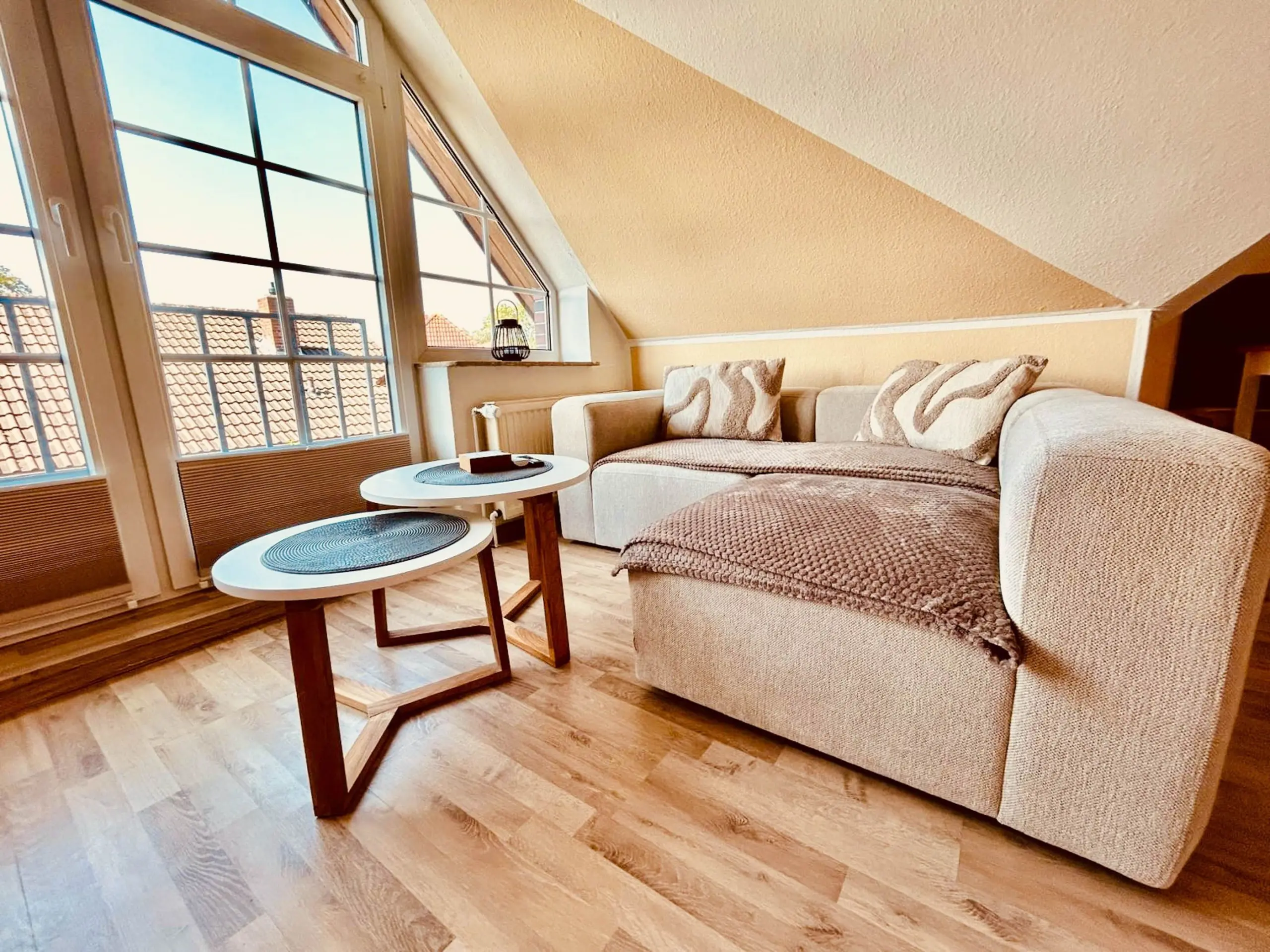 Sunlit living room with a large arched window, beige sofa, and round nesting coffee tables."