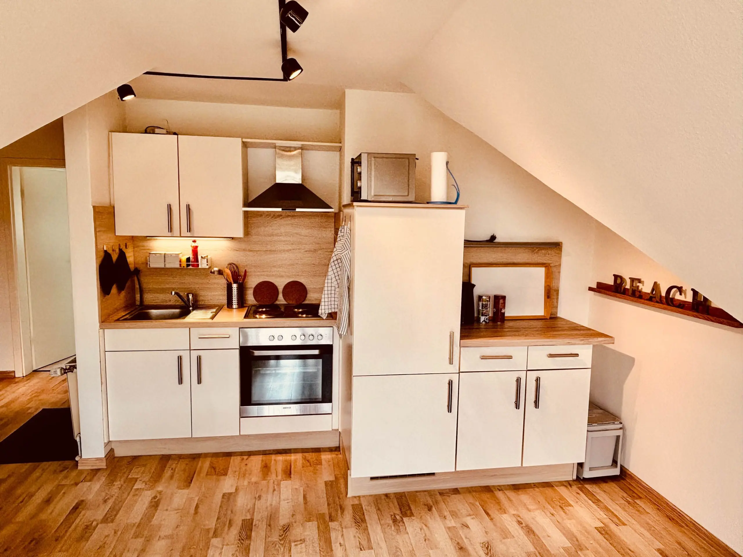 Modern white kitchen with built-in oven, induction hob, stainless range hood, and a microwave on a shelf above an island.