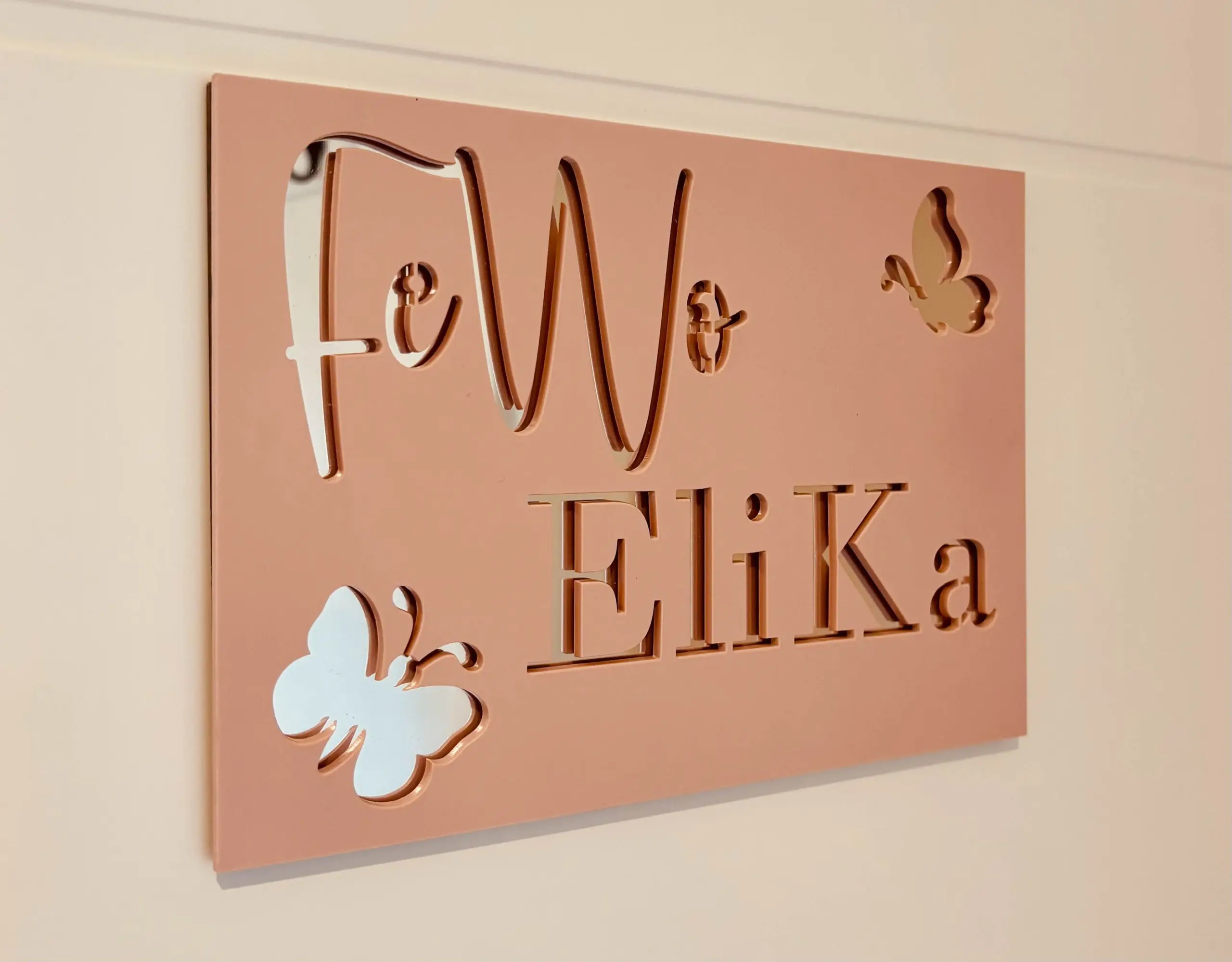 Pink metal wall plaque with raised cut-out letters and decorative white clouds in the bottom-left corner.