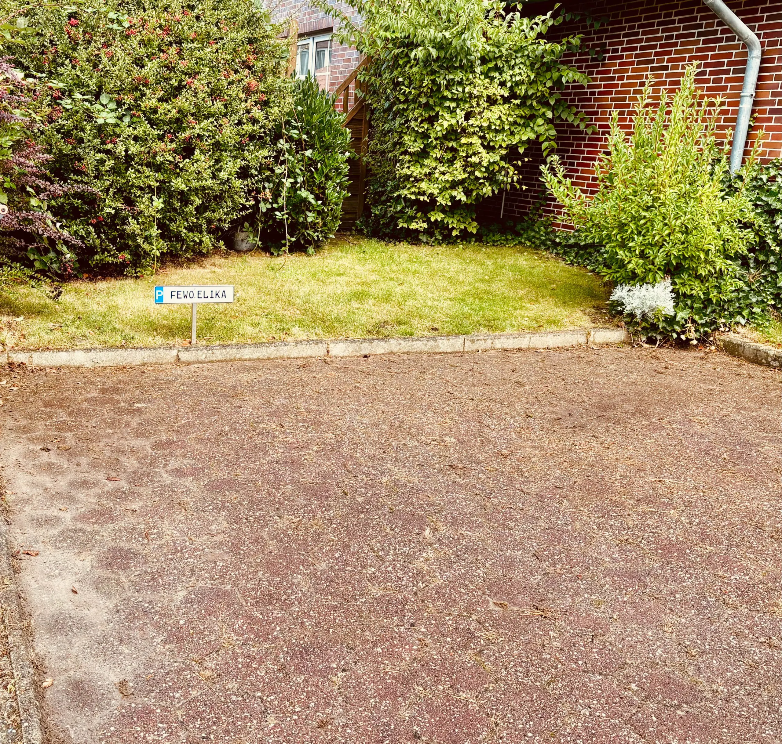 Small blue-and-white parking sign in a grassy area with dense shrubs and a brick building in the background.