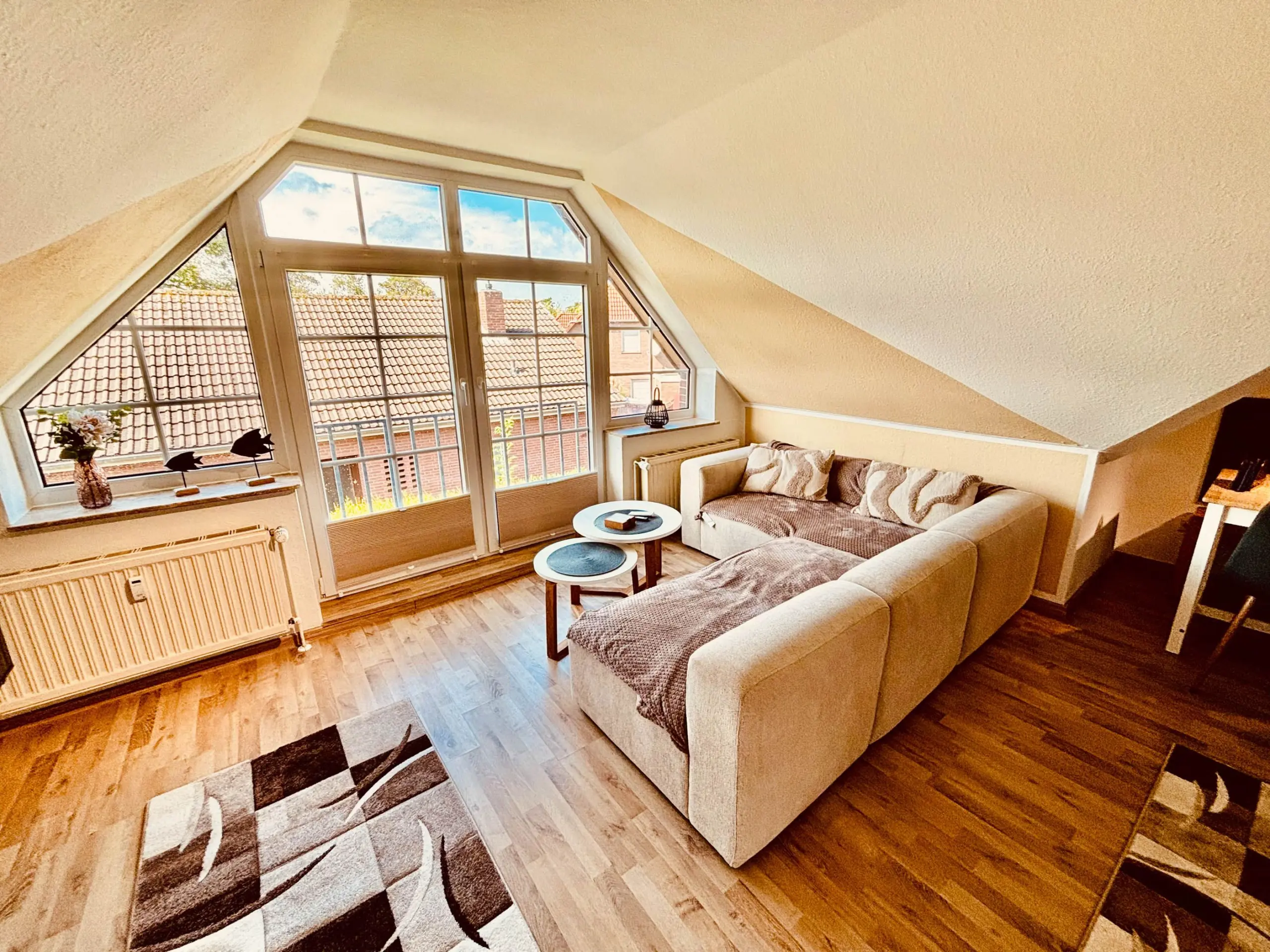 Cozy attic living room with a large triangular window, beige sofa, and patterned area rug.